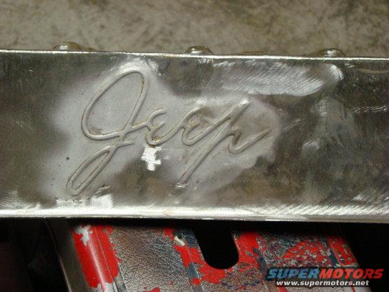 Close-up of a chrome Jeep emblem on a metal surface, with some scuff marks and a red and black object below