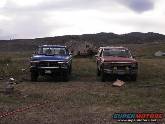 Blue 1977 Ford F-250 and red Ford Bronco parked in a grassy field