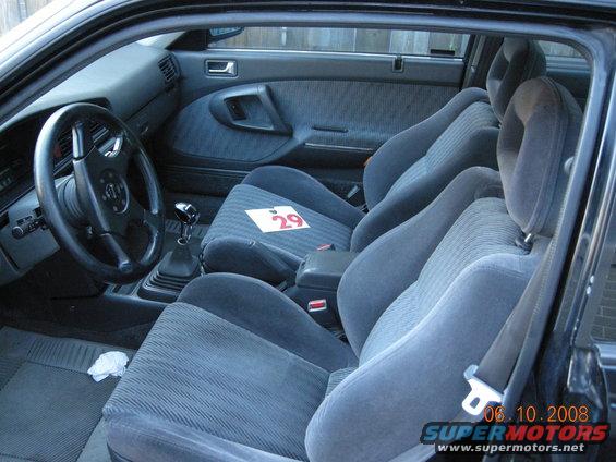 Interior view of a car showing front seats, dashboard, steering wheel, and gear shifter. A card with '29' is on the passenger seat