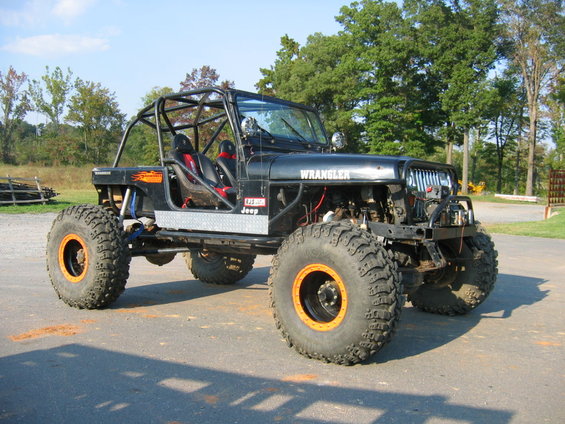Modified Jeep Wrangler with roll cage, large off-road tires, and orange wheel accents