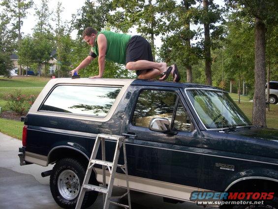 Dark green and tan SUV with a man cleaning its roof, ladder nearby