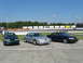 1993 Ford Taurus - Three Ford Taurus sedans are lined up in front of a racetrack, with the middle car being silver.