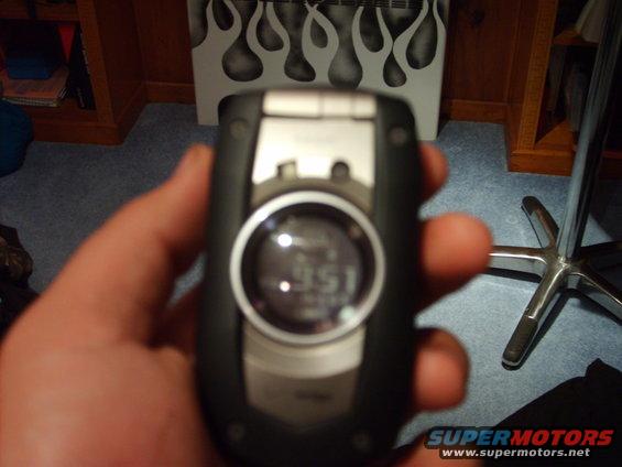 Hand holding a black flip phone showing '9:51' on its digital display