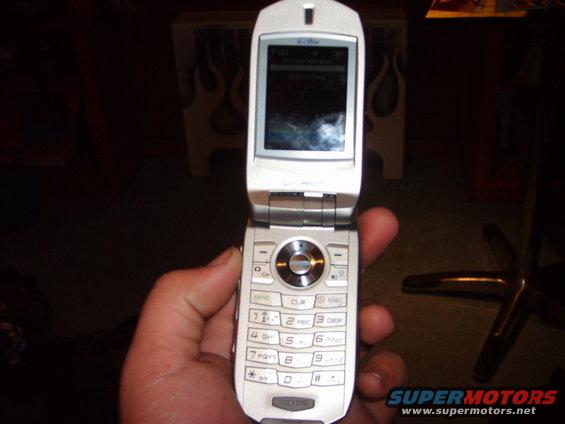 Silver flip phone held in a hand, showing the keypad and screen