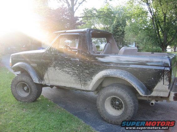 black SUV covered in mud, side view, sun glare on left