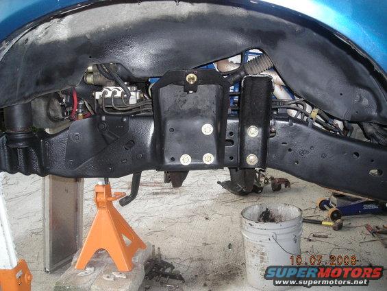 Close-up of vehicle frame and suspension parts on jack stands, with a bucket and tools nearby