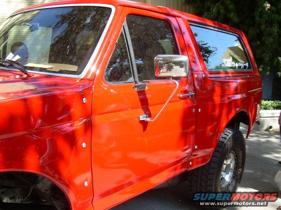 Red SUV with chrome side mirror and door handle, visible rivets along the body panels