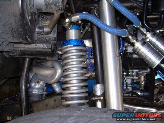 Close-up of off-road vehicle suspension with coilover shock, exhaust manifold, and blue hoses