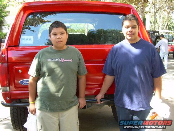Two boys stand in front of a red 1986 Ford Bronco. PIAA sticker on rear window