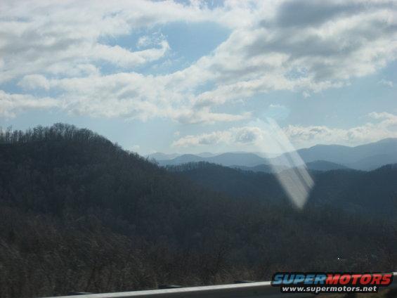 Mountain range under a cloudy sky, with a sunbeam reflection on the glass
