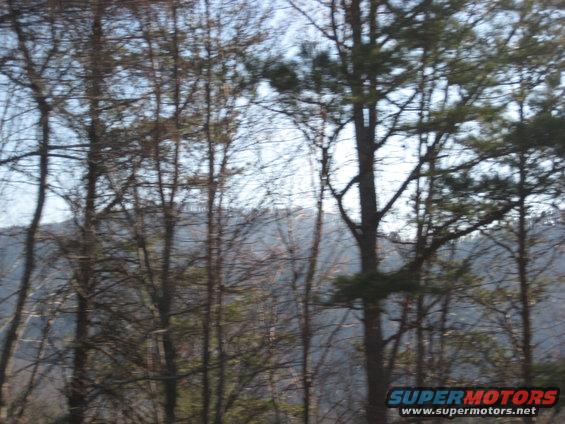 Trees and mountains under a hazy sky, with a 'SUPERMOTORS' watermark