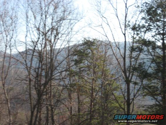 Trees and mountains under a bright sky, with a Supermotors logo in the lower right corner
