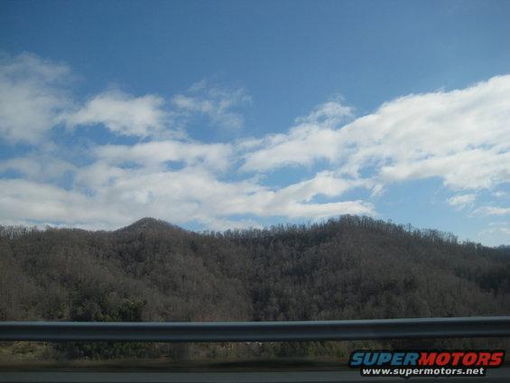 View of mountains and sky from a car window. Supermotors.net logo visible
