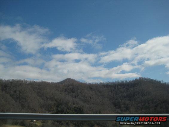 Mountain landscape with trees and clouds, highway guardrail in foreground