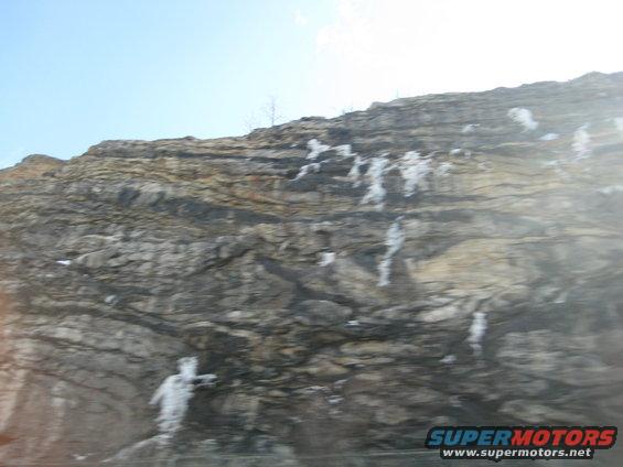 rocky cliff face with snow patches under a blue sky