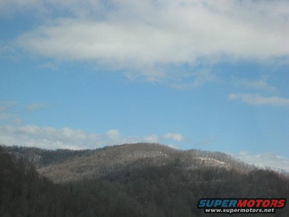 Mountains under a blue sky with clouds, Supermotors logo in corner