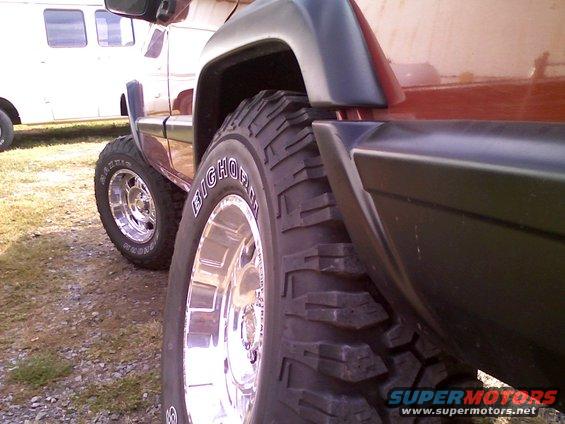 Side view of a 1998 Jeep Cherokee with large tires. Another vehicle is parked nearby