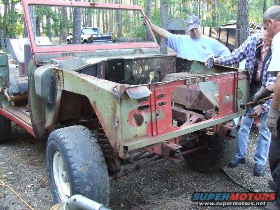 People working on a stripped-down Ford Bronco body, missing its hood and fenders