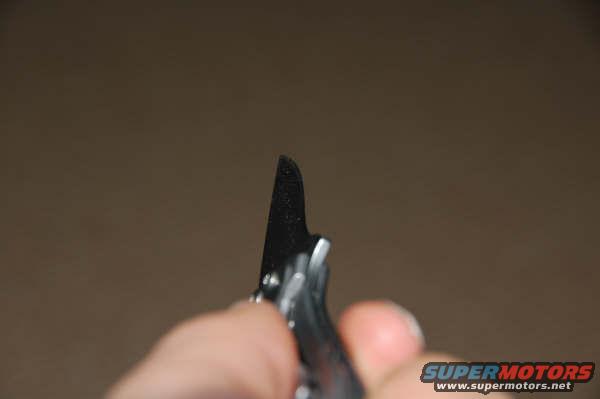 Close-up of a black tool blade with silver accents, held by a hand against a brown background