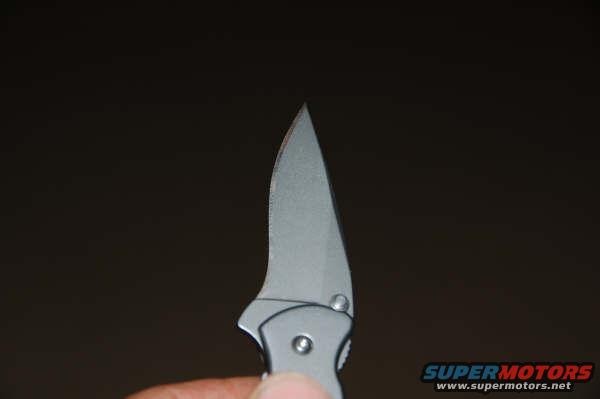 Folding knife with a silver blade and gray handle, held by a person's thumb and finger