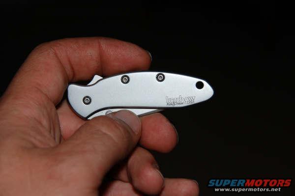 Silver Kershaw pocket knife with black handle, held in a hand against a dark background