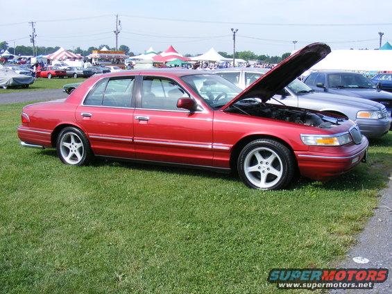 Red sedan with hood open, custom wheels, parked on grass