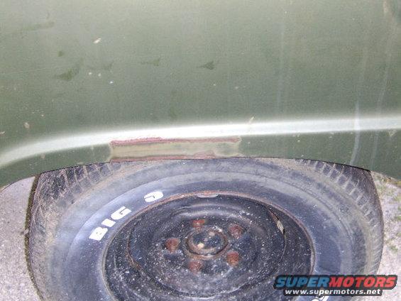Spare tire with white lettering and rusted fender section of a vehicle