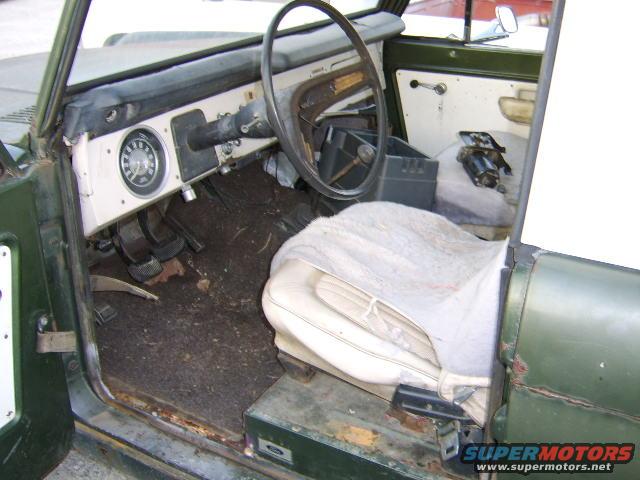 Green vehicle interior showing dashboard, steering wheel, pedals, and worn seat