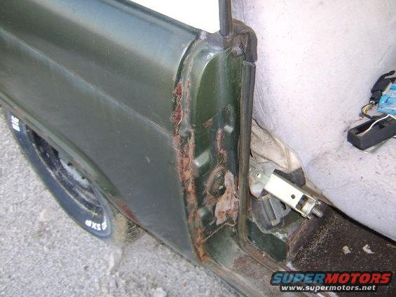 Green car door frame with significant rust around the hinge area and a portion of the interior seat visible