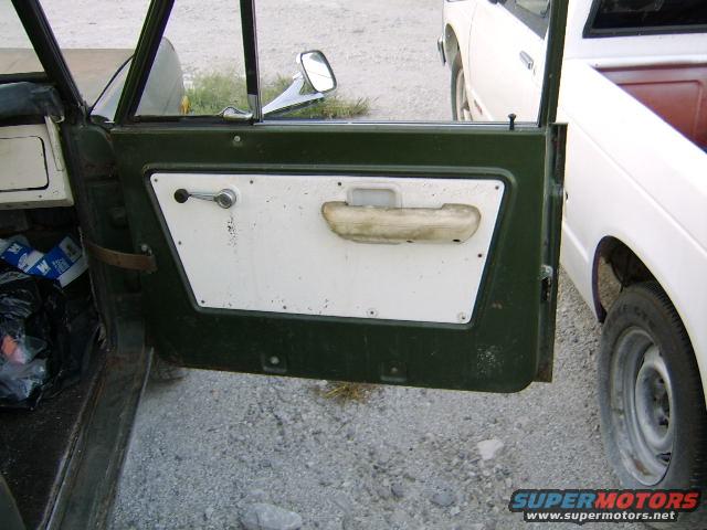 Open driver's door showing interior panel with handle and armrest, another vehicle visible outside