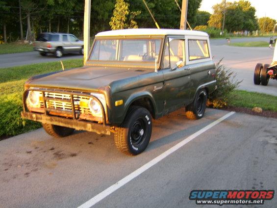 Green 1976 Ford Bronco parked in a lot, white top, aftermarket bumper