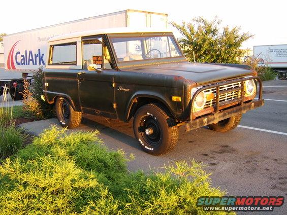 Dark green 1976 Ford Bronco with a white top, parked next to a CalArk trailer