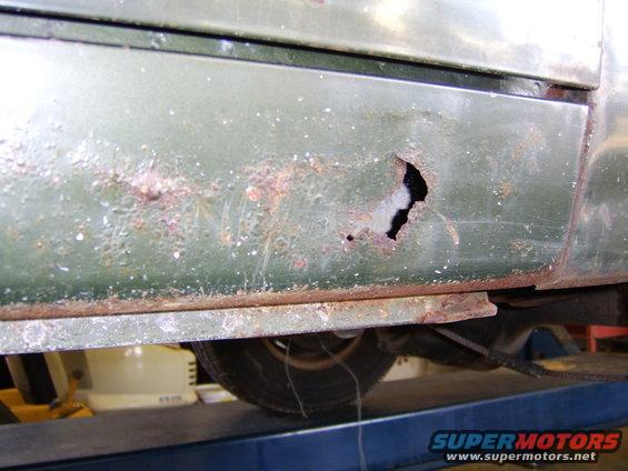 close-up of green vehicle's side rocker panel with a large rust hole