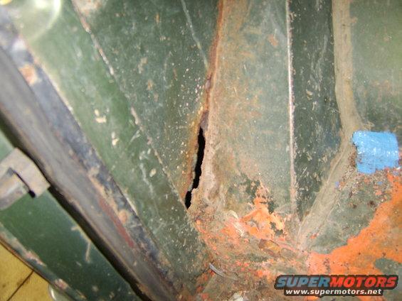 Rusted green metal panel with hole and orange undercoating