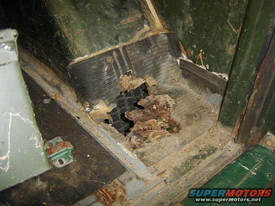 Close-up of a severely rusted floor pan with a hole showing the underside of a vehicle