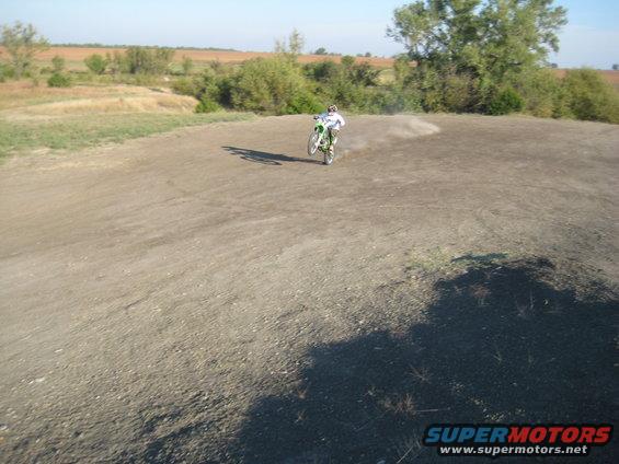 Dirt bike rider kicking up dust on a track. Supermotors.net logo in corner