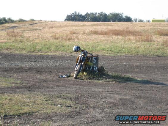 Yellow dirt bike with helmet on handlebars, leaning on a post marked 75 675