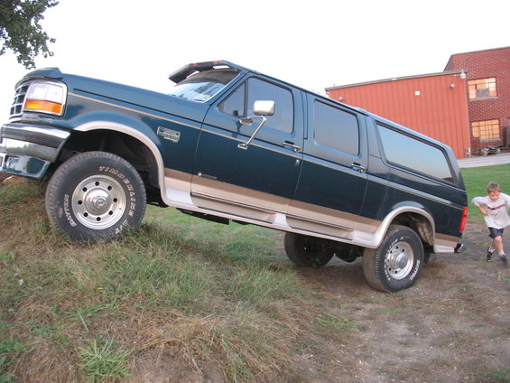 Green Ford extended SUV with tan trim on a grassy incline, kid running nearby