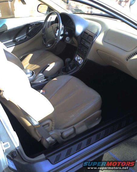 Car interior with tan seats, dashboard, steering wheel, and center console visible. Watermark says SUPERMOTORS.NET
