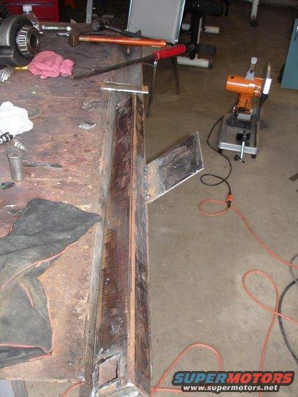 Welded metal frame piece on a workbench with tools and a chop saw in the background