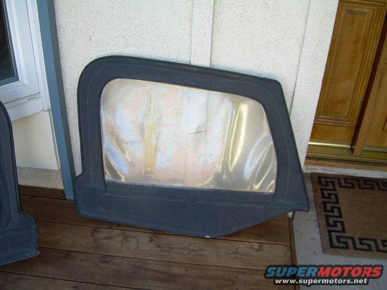 Black soft top window frame with clear plastic window, lying on wooden planks