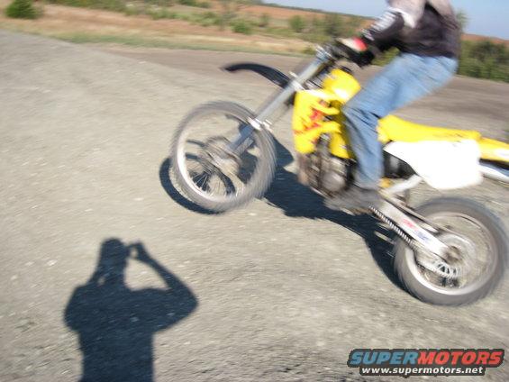 Person riding a yellow dirt bike on a dirt road, with their shadow visible