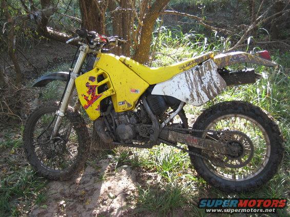 Yellow dirt bike covered in mud, parked in a wooded area