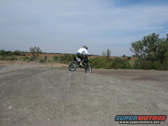 Green dirt bike with rider on a dirt track, number 27 visible