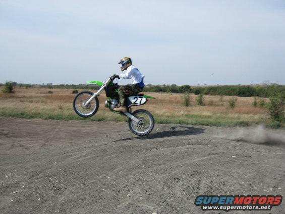 Dirt bike with number 27 on the side doing a wheelie on a dirt track