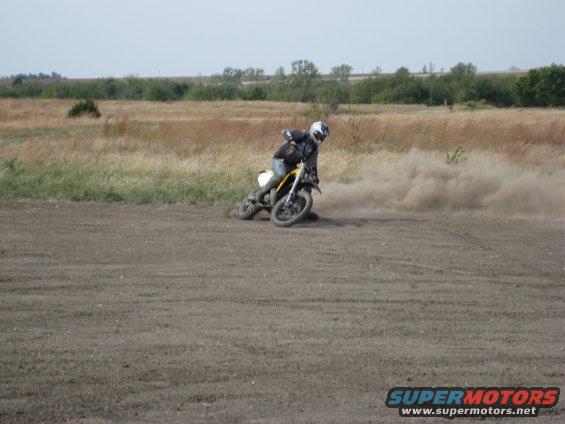 Dirt bike kicking up dust on a dirt track, rider wearing helmet and jacket
