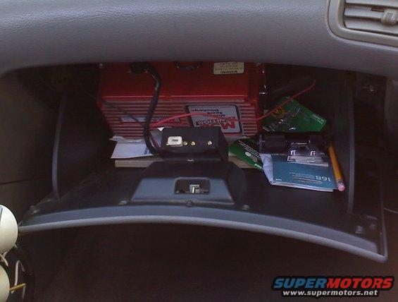 Glove compartment interior with red electronic box, black adapter, papers, and pencil