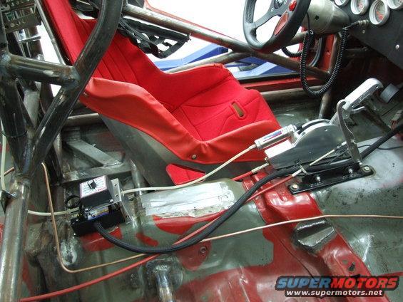 Racing car interior showing red bucket seat, roll cage, shifter, and gauges. SuperMotors logo visible