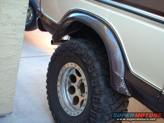Tan and brown 1978 Ford Bronco rear wheel with aftermarket chrome rim and off-road tire, close-up side view