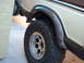 1978 Ford Bronco - Close-up of the rear wheel and fender flare of a tan and brown 1978 Ford Bronco, showing aftermarket wheels and tires.